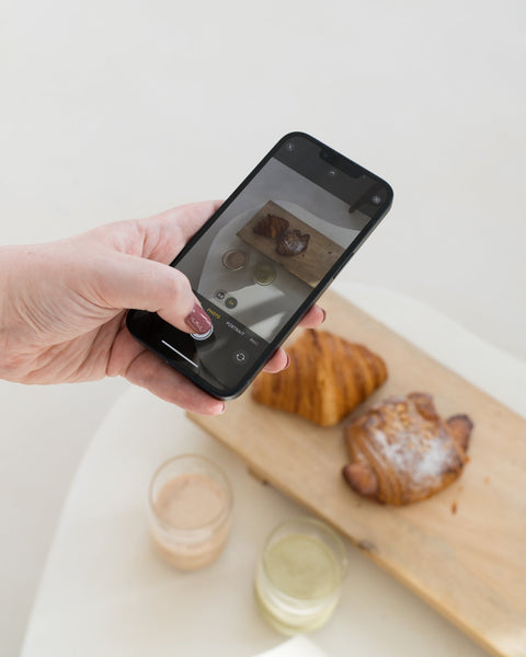 Hand holding a smartphone taking a photo of pastries on a wooden board.